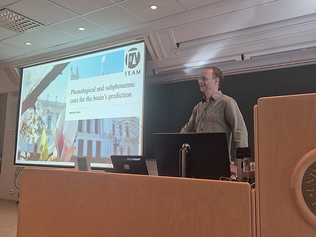 Mikael is standing in front of a screen showing a powerpoint presentation. He is smiling at an audience.